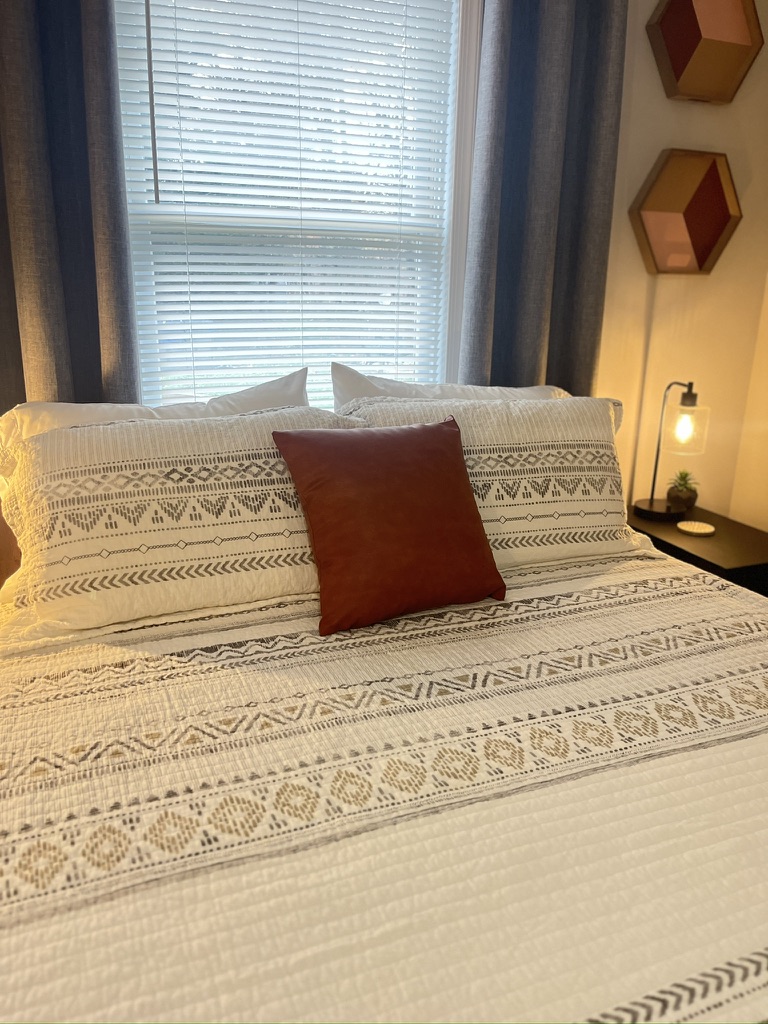 Bed dressed with patterned linens and a leather accent pillow