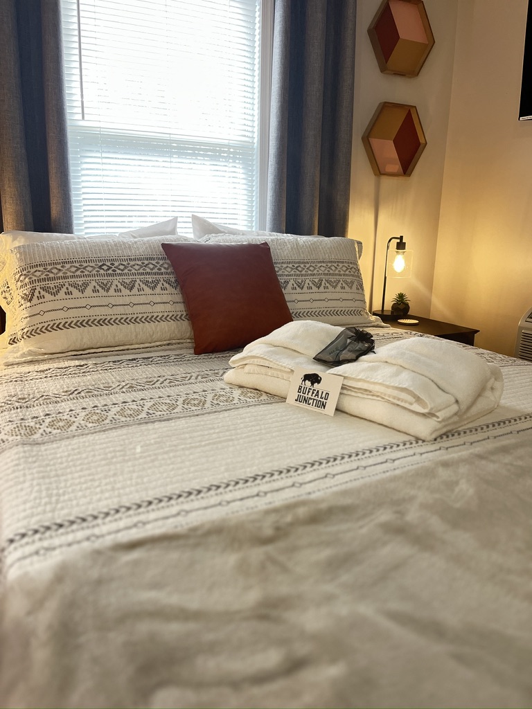 Bed with welcome towels in front of a bright window