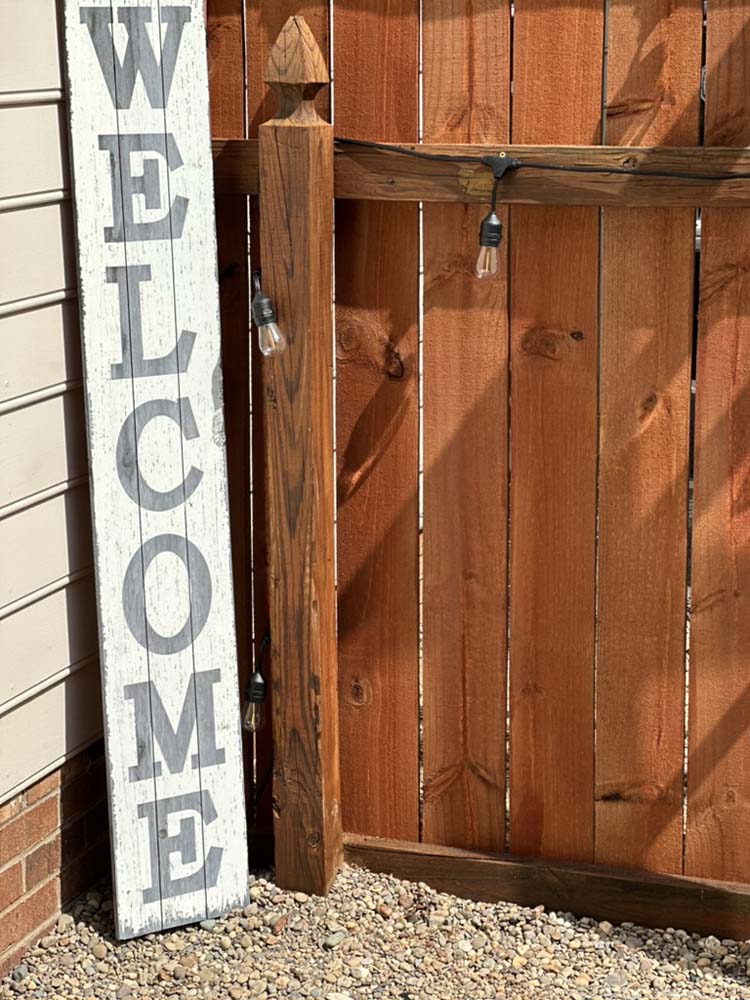 Rustic ‘Welcome’ sign by the wooden gate and string lights